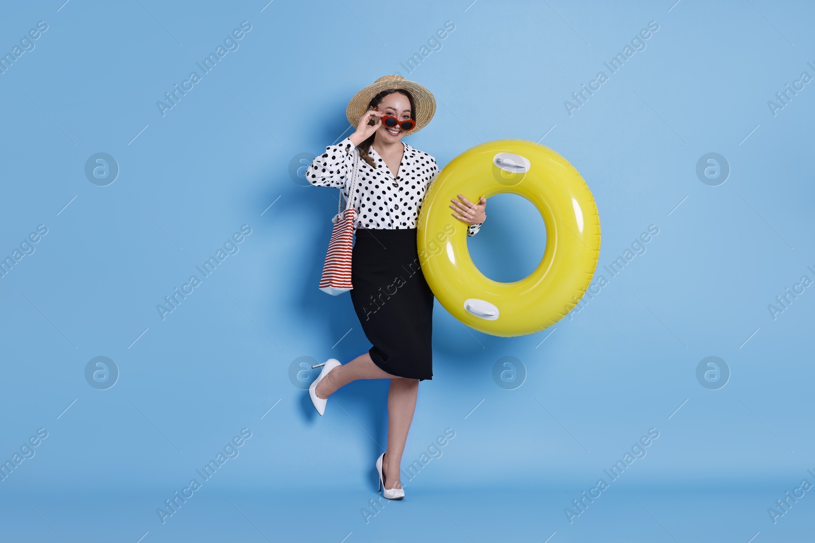 Photo of Businesswoman with inflatable ring, straw hat, bag and sunglasses on light blue background