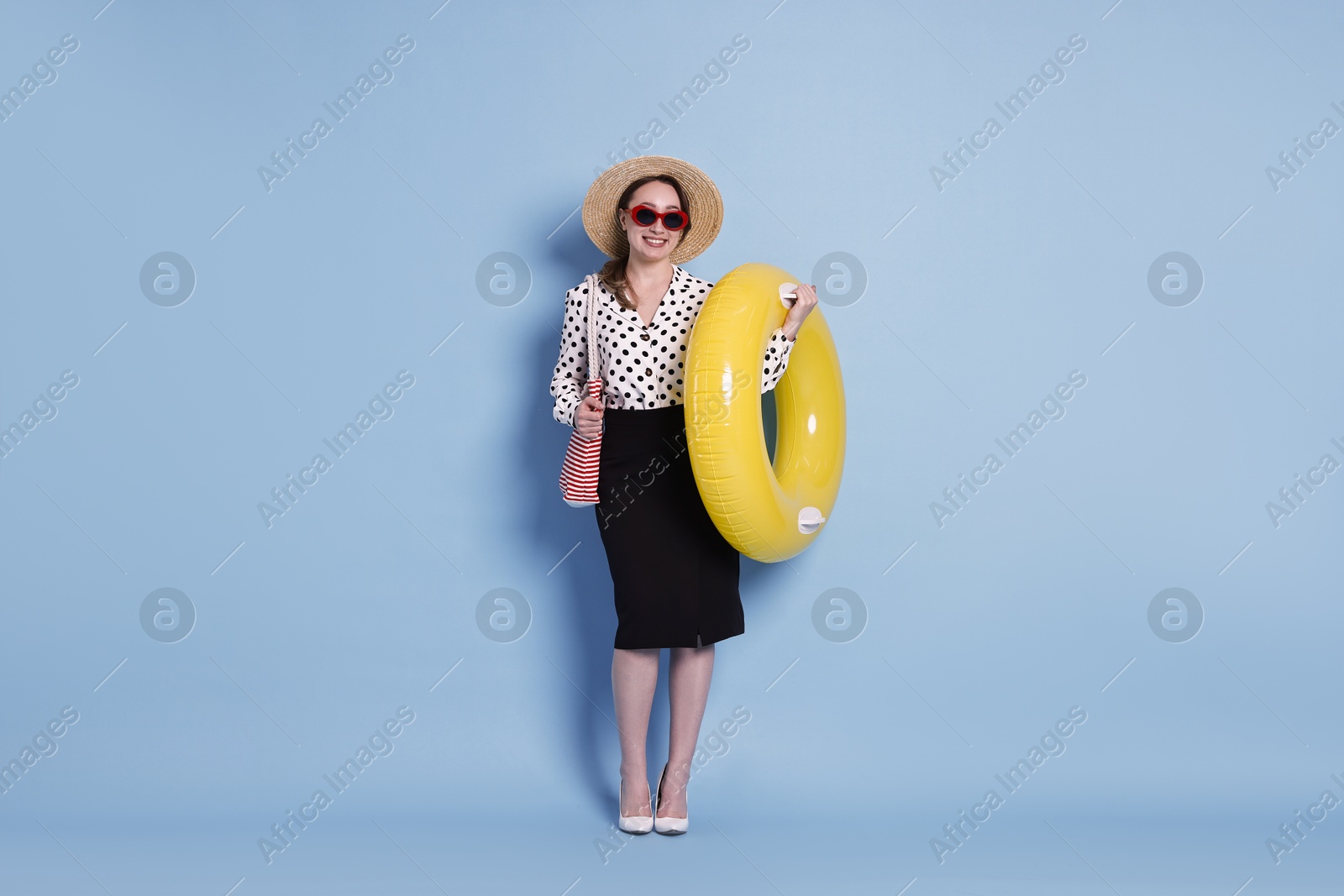 Photo of Businesswoman with inflatable ring, straw hat, bag and sunglasses on light blue background