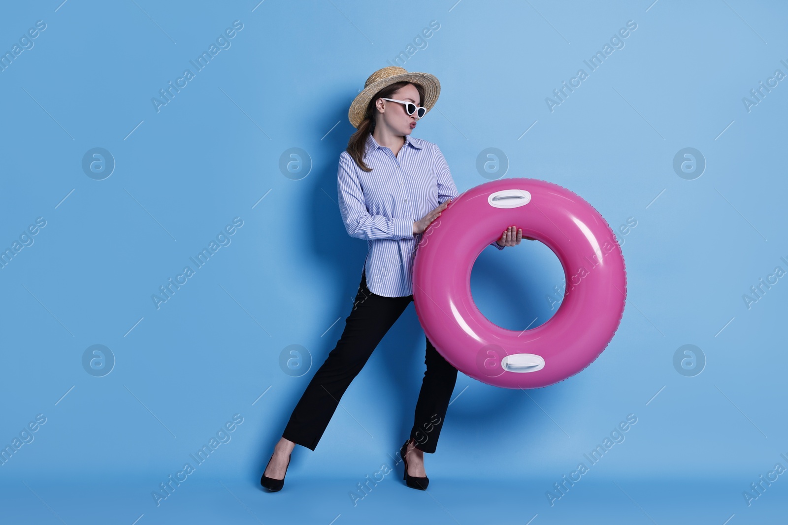 Photo of Businesswoman with inflatable ring, straw hat and sunglasses on light blue background