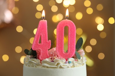 Photo of 40th birthday. Tasty cake with burning number shaped candles and sprinkles on blurred background with lights, closeup. Bokeh effect