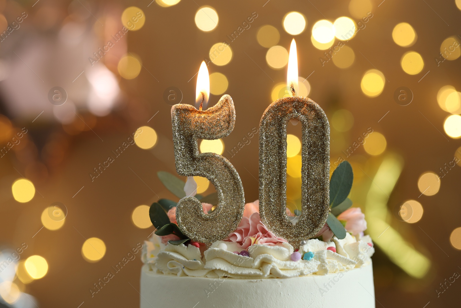 Photo of 50th birthday. Tasty cake with burning number shaped candles and sprinkles on blurred background with lights, closeup. Bokeh effect