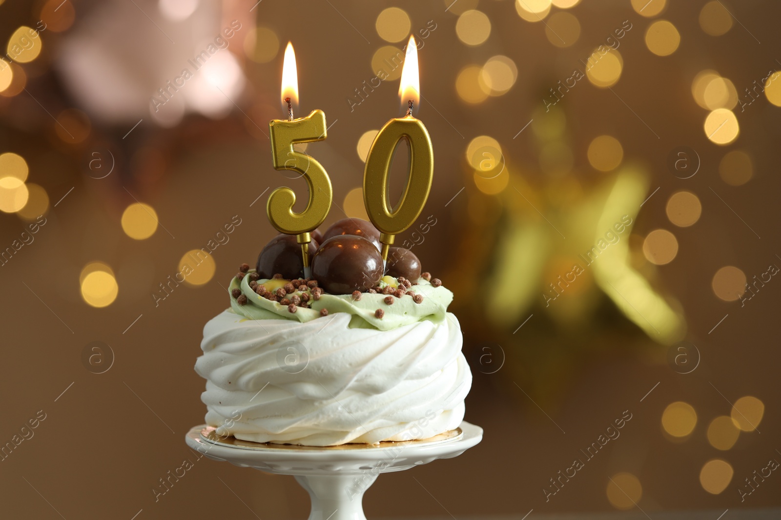 Photo of 50th birthday. Tasty cupcake with burning number shaped candles on blurred background with lights, closeup. Bokeh effect