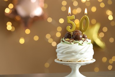 Photo of 50th birthday. Tasty cupcake with burning number shaped candles on blurred background with lights, space for text. Bokeh effect