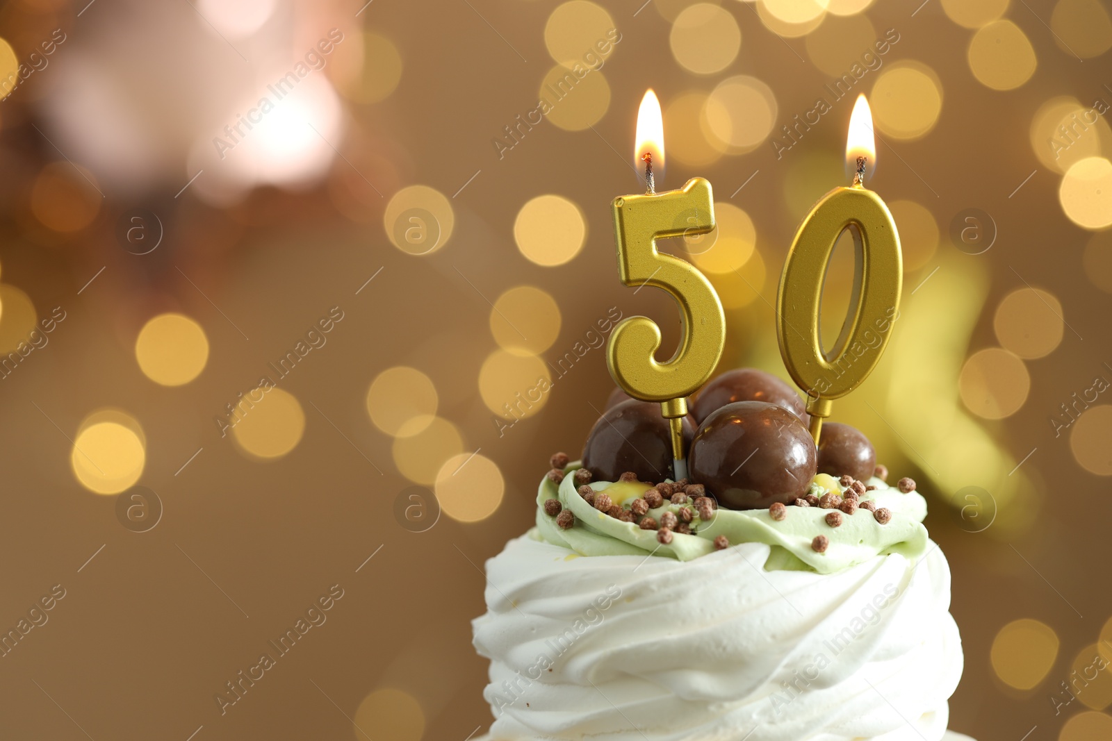 Photo of 50th birthday. Tasty cupcake with burning number shaped candles on blurred background with lights, space for text. Bokeh effect