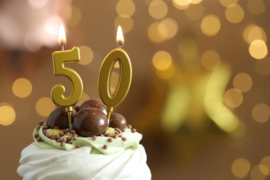 Photo of 50th birthday. Tasty cupcake with burning number shaped candles on blurred background with lights, space for text. Bokeh effect