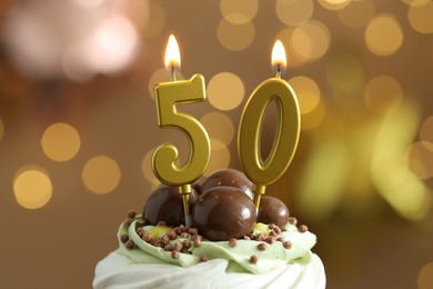 Photo of 50th birthday. Tasty cupcake with burning number shaped candles on blurred background with lights, closeup. Bokeh effect