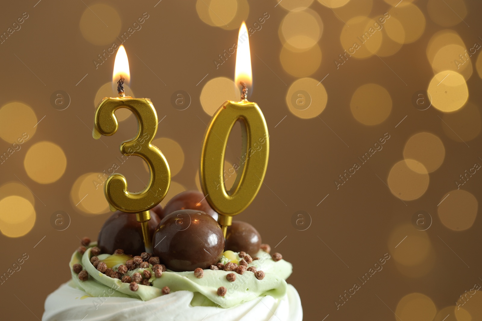 Photo of 30th birthday. Tasty cupcake with burning number shaped candles on blurred background with lights, space for text. Bokeh effect