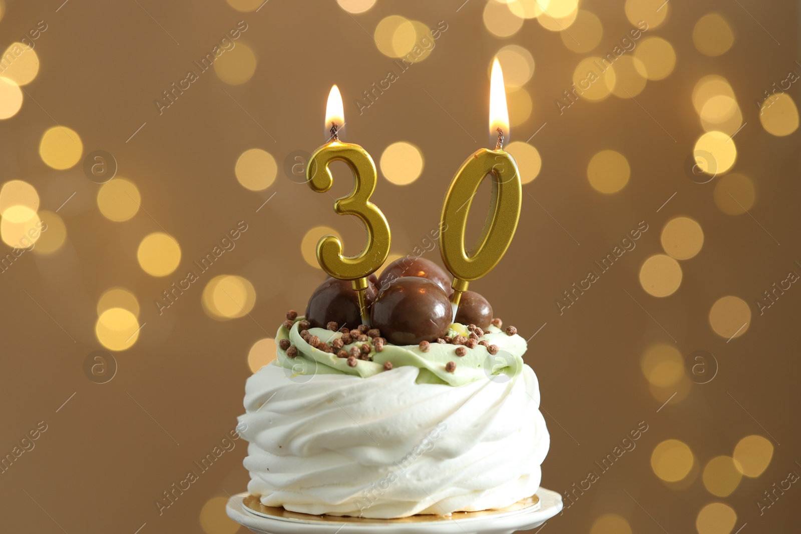 Photo of 30th birthday. Tasty cupcake with burning number shaped candles on blurred background with lights, closeup. Bokeh effect