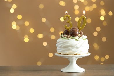 Photo of 30th birthday. Tasty cupcake with burning number shaped candles on wooden table against blurred background with lights, space for text. Bokeh effect