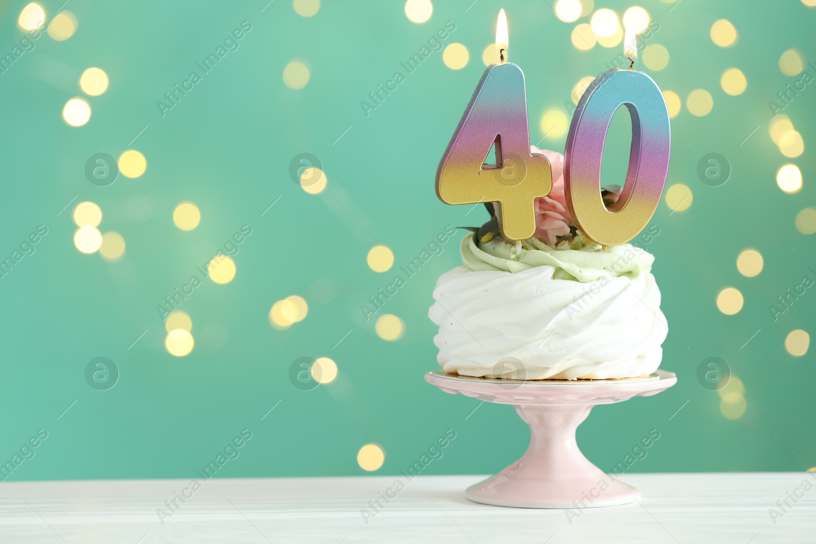 Photo of 40th birthday. Tasty cupcake with burning number shaped candles on white wooden table against turquoise background with blurred lights, space for text. Bokeh effect