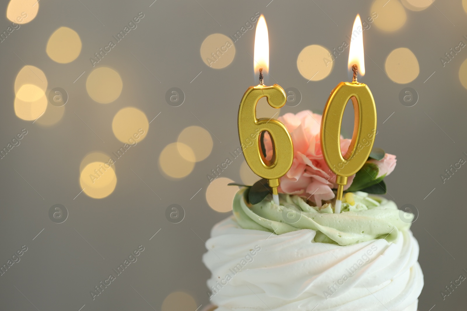 Photo of 60th birthday. Tasty cupcake with burning number shaped candles on grey background with blurred lights, closeup. Bokeh effect