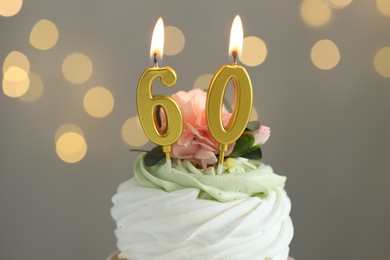 Photo of 60th birthday. Tasty cupcake with burning number shaped candles on grey background with blurred lights, closeup. Bokeh effect