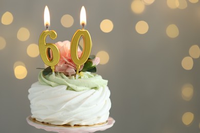 Photo of 60th birthday. Tasty cupcake with burning number shaped candles on grey background with blurred lights, space for text. Bokeh effect