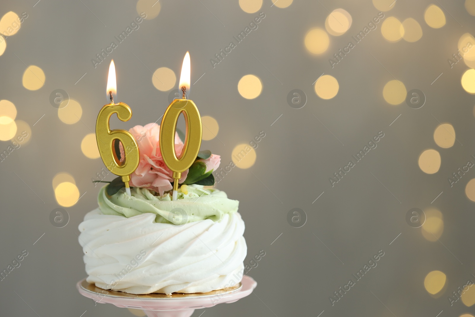 Photo of 60th birthday. Tasty cupcake with burning number shaped candles on grey background with blurred lights, space for text. Bokeh effect