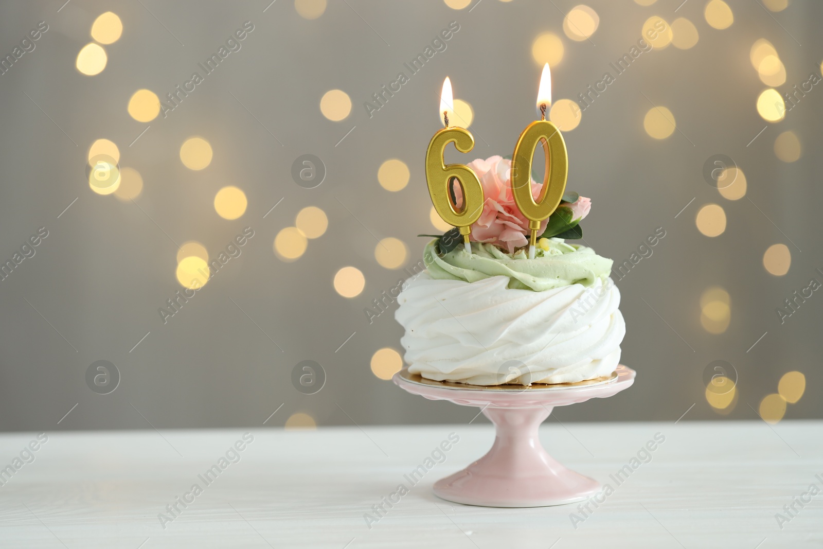 Photo of 60th birthday. Tasty cupcake with burning number shaped candles on white wooden table against grey background with blurred lights, space for text. Bokeh effect