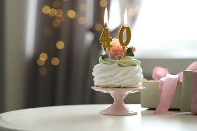 Photo of 40th birthday. Tasty cupcake with burning number shaped candles and gift boxes on table against blurred background with lights, space for text. Bokeh effect