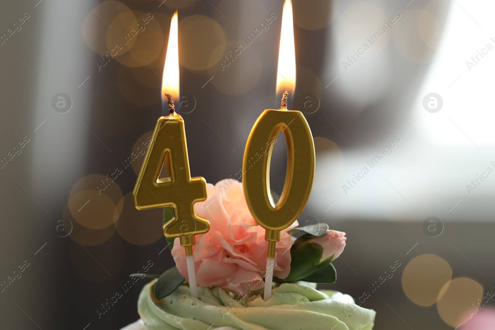 Photo of 40th birthday. Tasty cupcake with burning number shaped candles on blurred background with lights, closeup. Bokeh effect