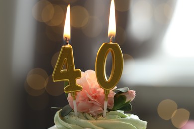 Photo of 40th birthday. Tasty cupcake with burning number shaped candles on blurred background with lights, closeup. Bokeh effect