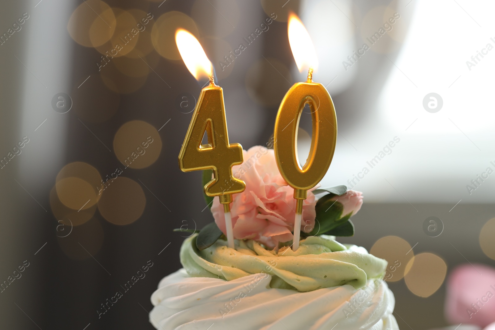 Photo of 40th birthday. Tasty cupcake with burning number shaped candles on blurred background with lights, closeup. Bokeh effect