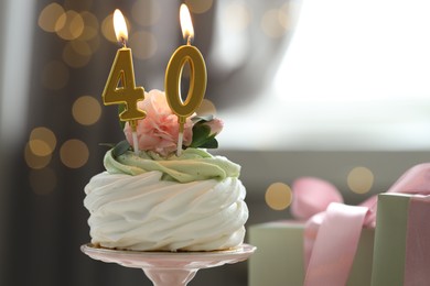 Photo of 40th birthday. Tasty cupcake with burning number shaped candles and gift boxes on blurred background with lights, closeup. Bokeh effect