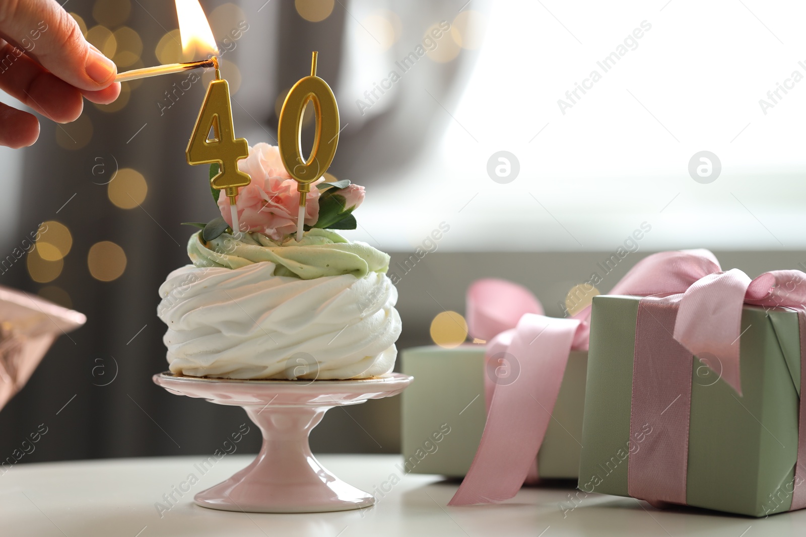 Photo of 40th birthday. Woman lighting number shaped candles on cupcake at table against blurred background with lights, closeup. Bokeh effect