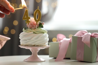 Photo of 40th birthday. Woman lighting number shaped candles on cupcake at table against blurred background with lights, closeup. Bokeh effect