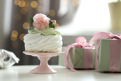 Photo of Tasty cupcake with floral decor and gift boxes on table against blurred background with lights, bokeh effect