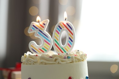 Photo of 30th birthday. Tasty cake with burning number shaped candles and sprinkles on blurred background with lights, closeup. Bokeh effect