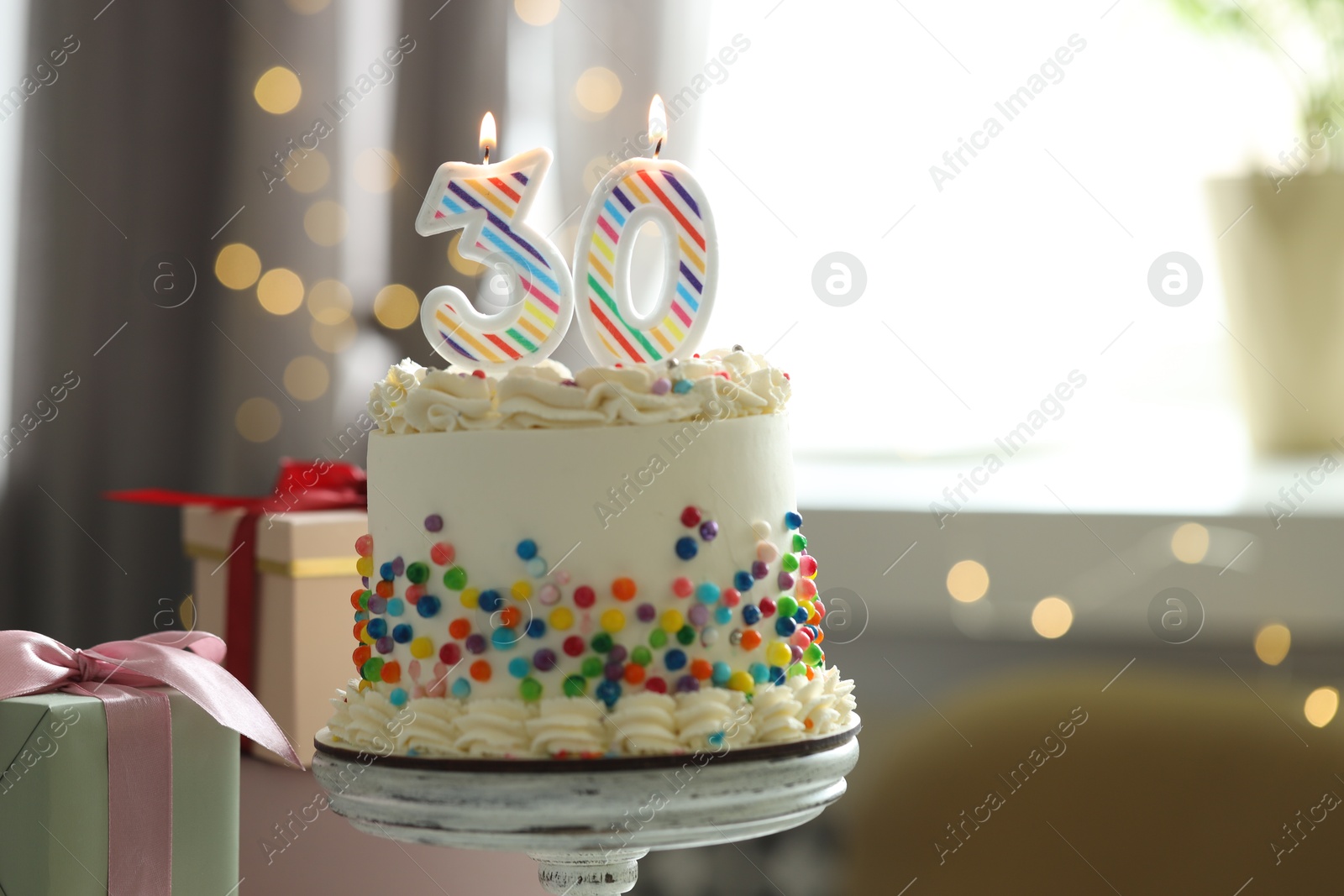 Photo of 30th birthday. Tasty cake with burning number shaped candles, sprinkles and gift boxes on blurred background with lights, space for text. Bokeh effect