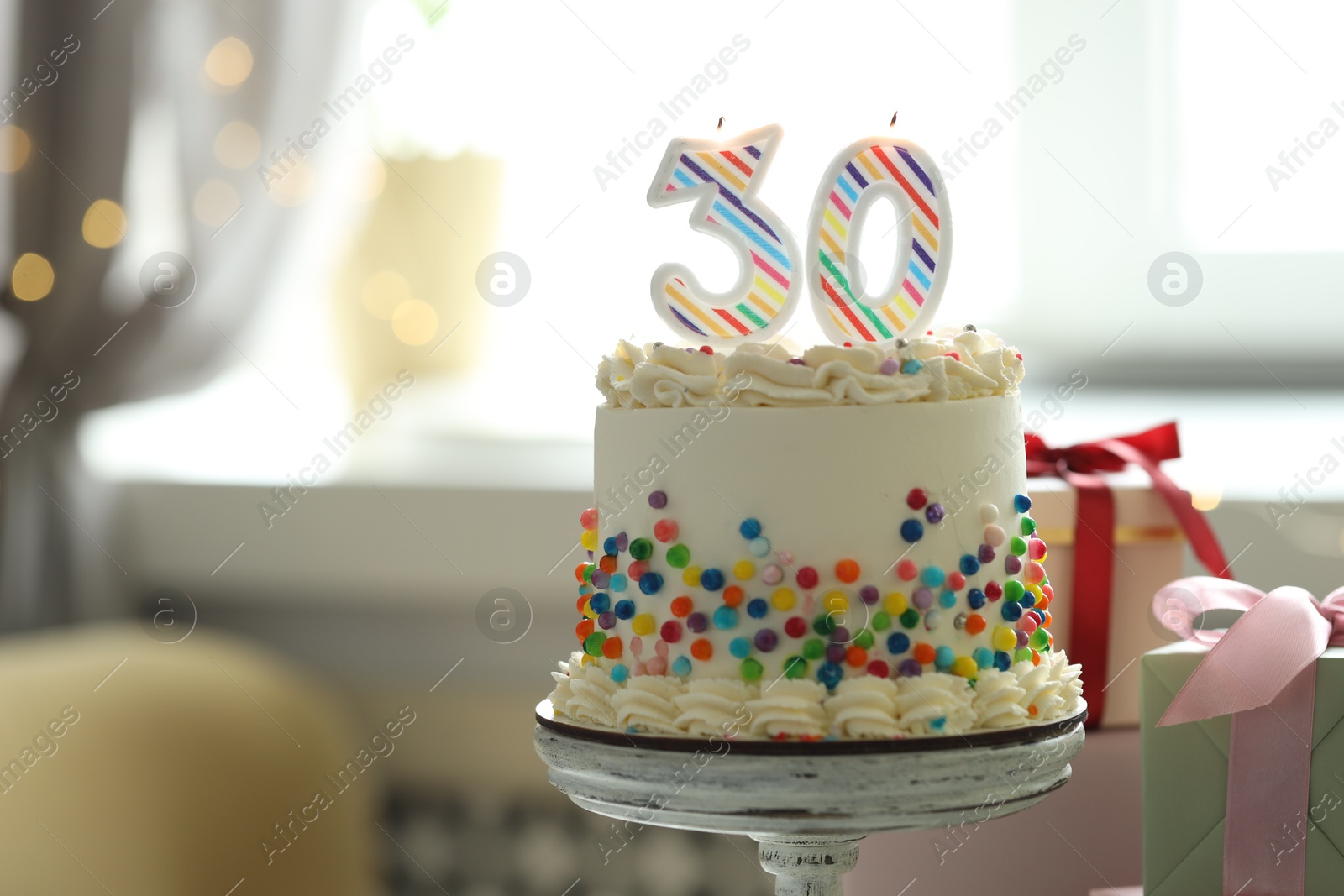 Photo of 30th birthday. Tasty cake with burning number shaped candles, sprinkles and gift boxes on blurred background with lights, space for text. Bokeh effect