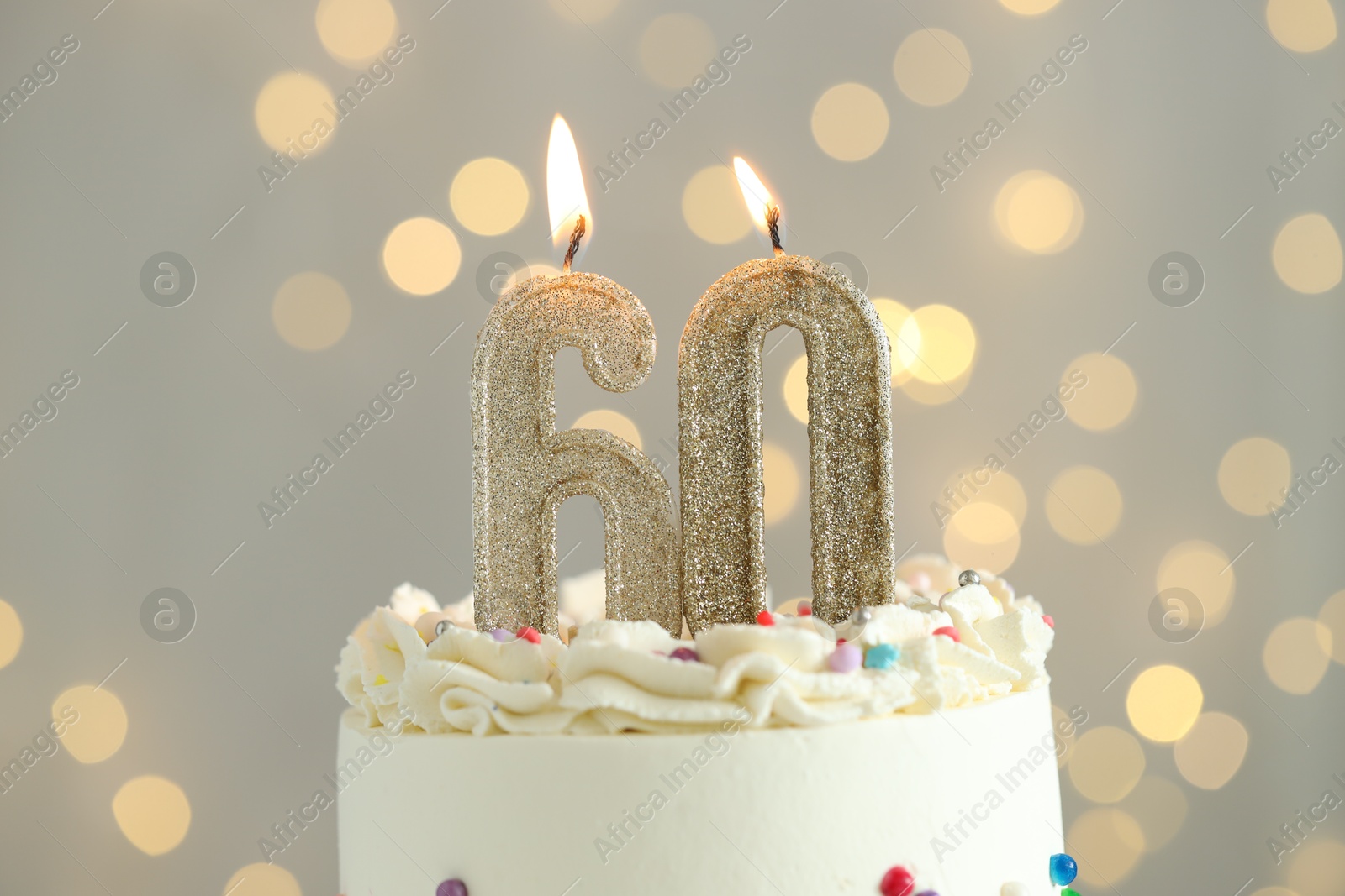 Photo of 60th birthday. Tasty cake with burning number shaped candles and sprinkles on grey background with blurred lights, closeup. Bokeh effect