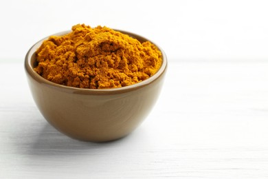 Photo of Turmeric powder in bowl on white wooden table, closeup. Space for text