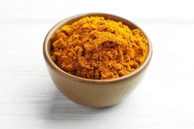 Photo of Turmeric powder in bowl on white wooden table, closeup