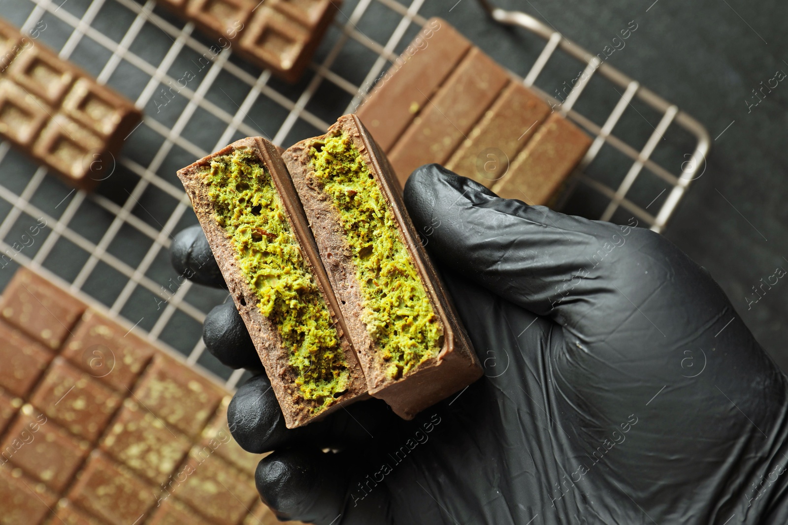 Photo of Woman holding pieces of delicious Dubai chocolate with pistachios and knafeh at table, top view