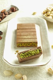 Photo of Pieces of delicious Dubai chocolate with pistachios, knafeh and cocoa beans on light textured table, closeup