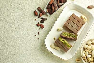 Photo of Pieces of delicious Dubai chocolate with pistachios, knafeh and cocoa beans on light textured table, flat lay. Space for text