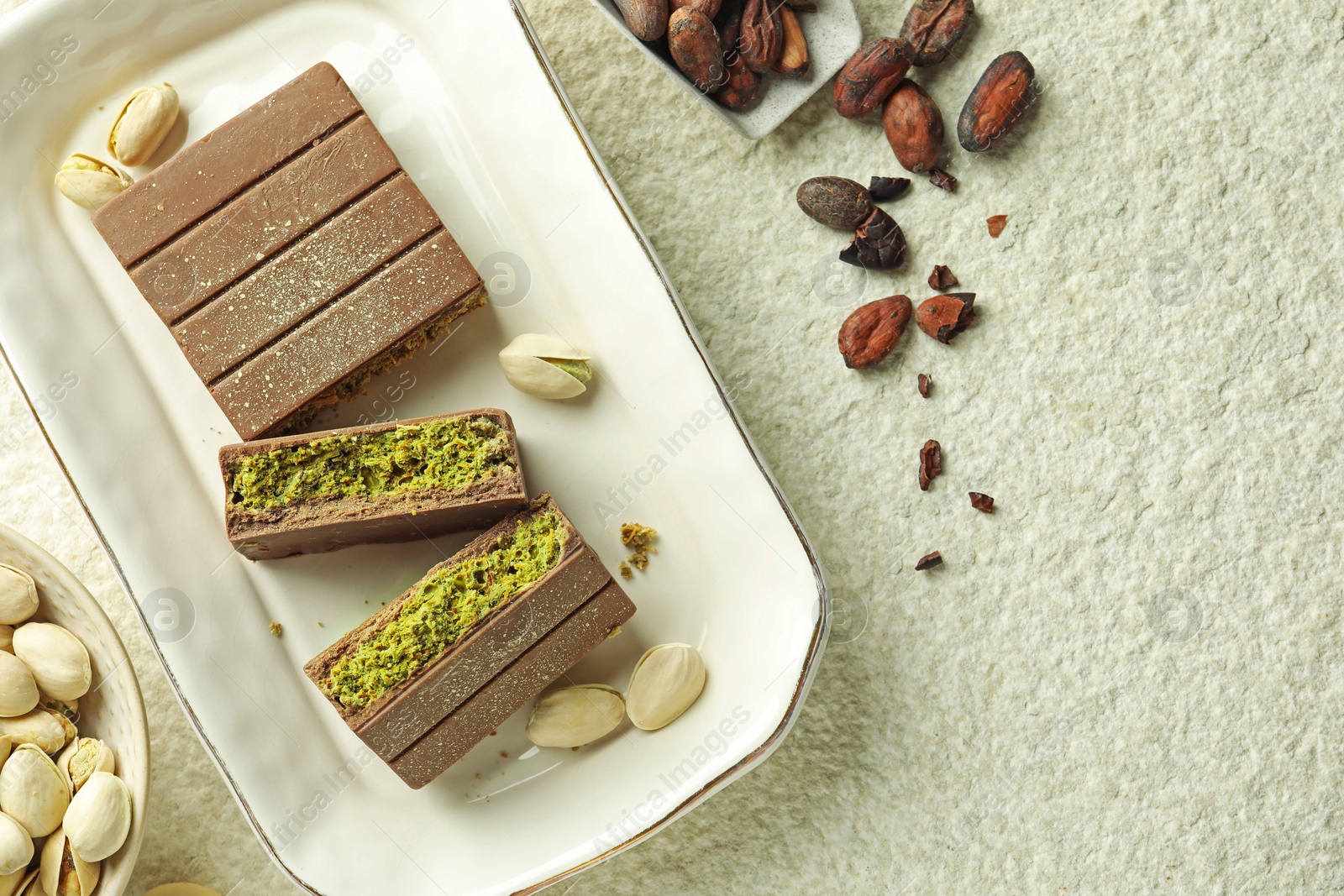 Pieces of delicious Dubai chocolate with pistachios, knafeh and cocoa beans on light textured table, flat lay. Space for text Photo of Pieces of delicious Dubai chocolate with pistachios, knafeh and cocoa beans on light textured table, flat lay. Space for text