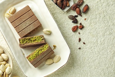 Photo of Pieces of delicious Dubai chocolate with pistachios, knafeh and cocoa beans on light textured table, flat lay. Space for text