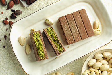 Photo of Pieces of delicious Dubai chocolate with pistachios, knafeh and cocoa beans on light textured table, flat lay