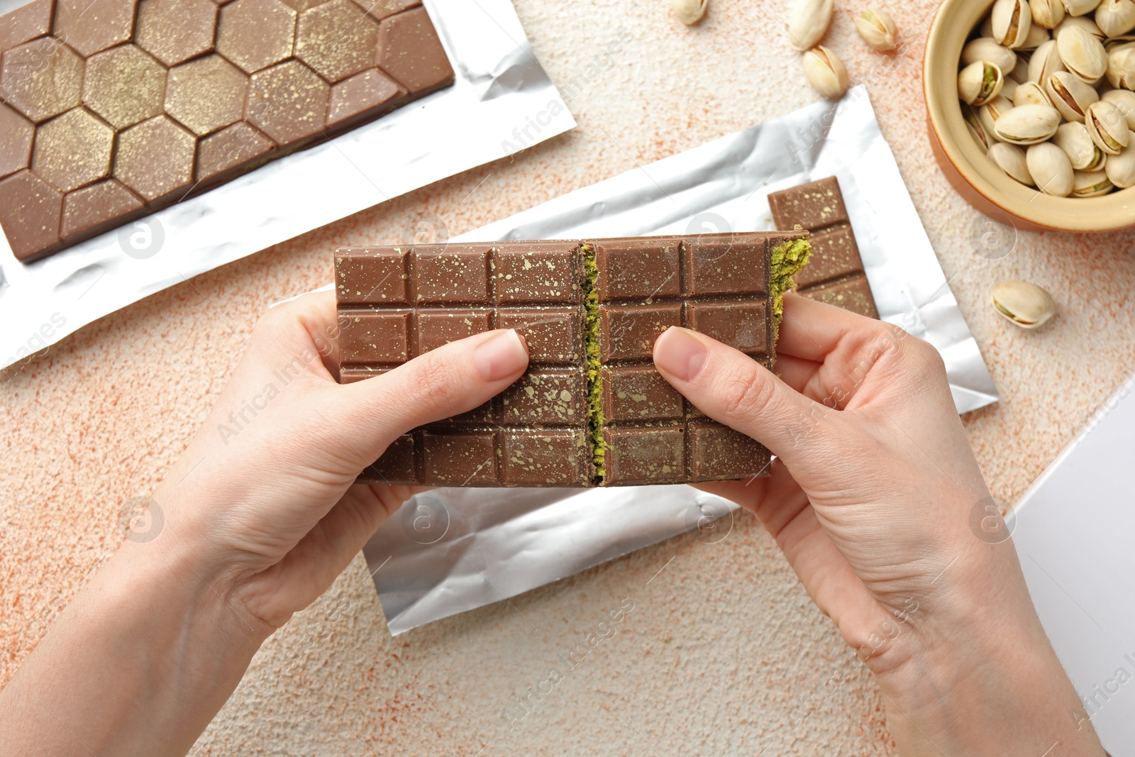 Photo of Woman breaking delicious Dubai chocolate bar with pistachios and knafeh at color textured table, top view