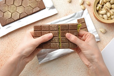 Photo of Woman breaking delicious Dubai chocolate bar with pistachios and knafeh at color textured table, top view