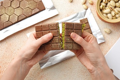 Woman breaking delicious Dubai chocolate bar with pistachios and knafeh at color textured table, top view