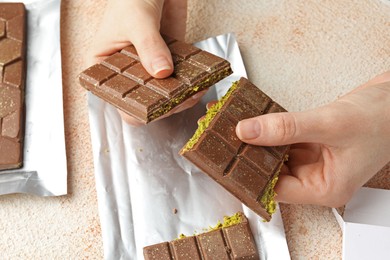 Woman breaking delicious Dubai chocolate bar with pistachios and knafeh at color textured table, above view