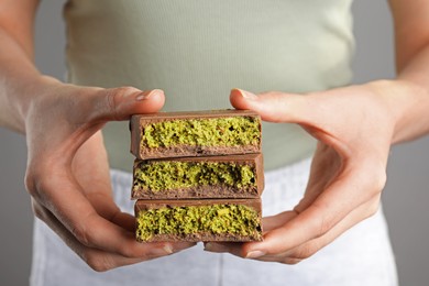 Photo of Woman holding pieces of delicious Dubai chocolate with pistachios and knafeh on grey background, closeup