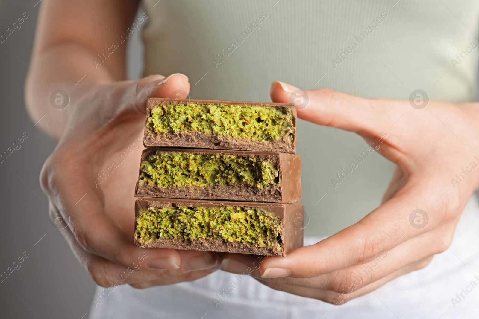 Photo of Woman holding pieces of delicious Dubai chocolate with pistachios and knafeh on grey background, closeup