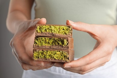 Photo of Woman holding pieces of delicious Dubai chocolate with pistachios and knafeh on grey background, closeup