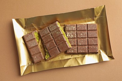 Photo of Pieces of delicious Dubai chocolate with pistachios and knafeh on dark beige background, top view