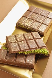 Photo of Pieces of delicious Dubai chocolate with pistachios and knafeh on dark beige background, closeup