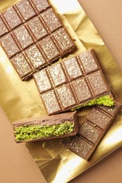 Photo of Pieces of delicious Dubai chocolate with pistachios and knafeh on dark beige background, top view