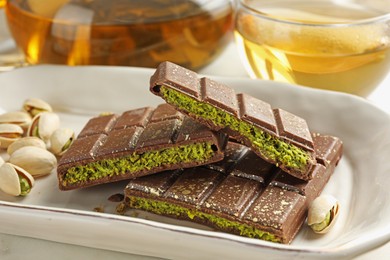 Photo of Pieces of delicious Dubai chocolate with pistachios, knafeh and tea on table, closeup